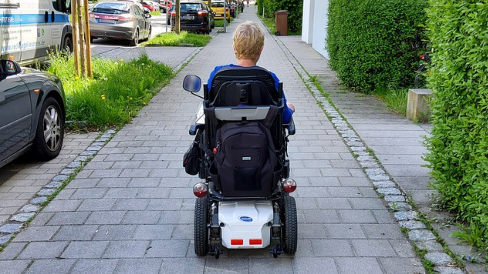 Mujer en silla de ruedas de espaldas, avanzando por una acera