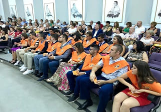 Grupo de estudiantes universitarios, sentados en un auditorio, con orlas naranjas