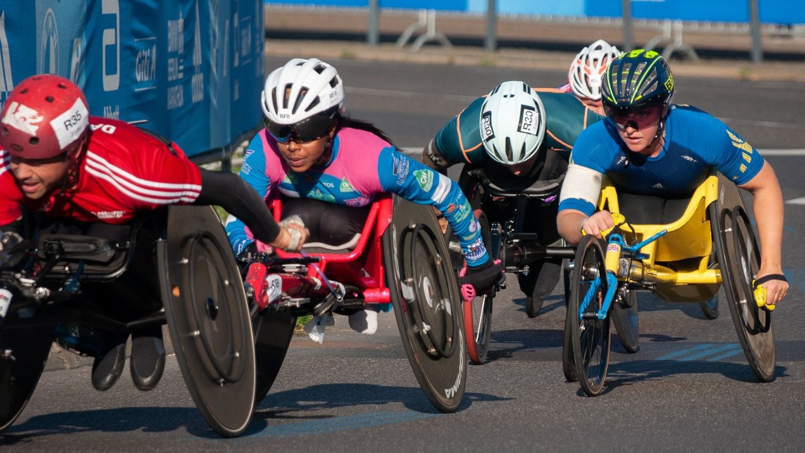 Personas en sillas de ruedas compitiendo en una carrera sobre una pista de asfalto